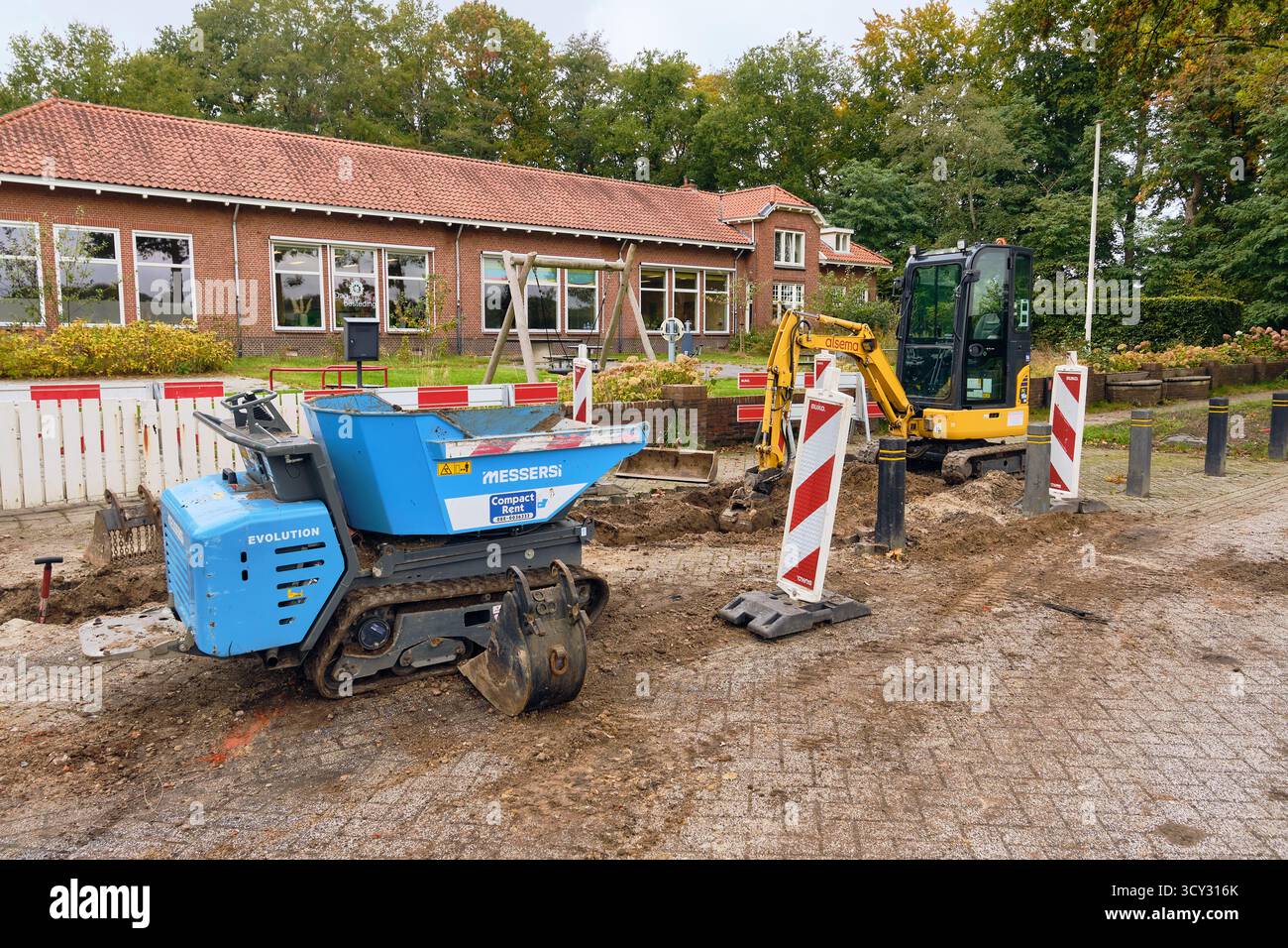 Roden, Niederlande; 08. Oktober 2025: Ein gelber Komatsu Minibagger und ein blauer Messersi-Dumper führen Grabenverfüllung und Straßenreparaturen an einer Straße durch Stockfoto