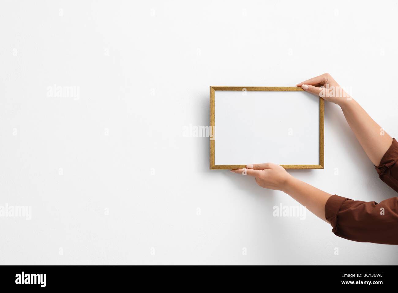 Frau, die einen leeren Diplomrahmen an der weißen Wand hängt, Großaufnahme. Modell für Design Stockfoto