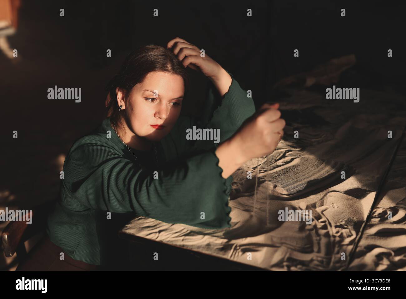 Kreative Frau streut Sand in einem schwach beleuchteten Raum mit Schatten Stockfoto