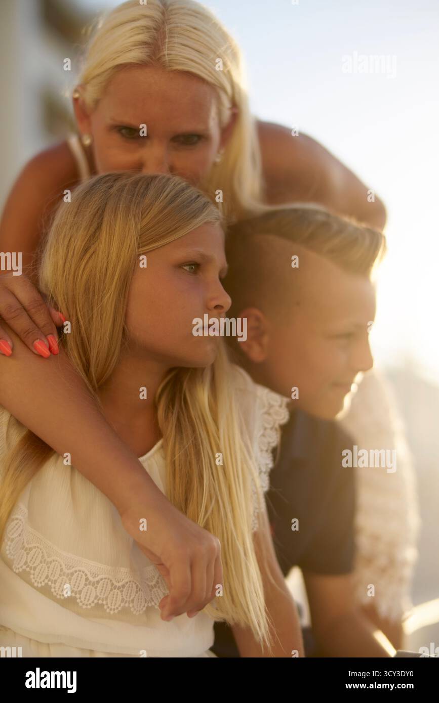 Liebevolle alleinerziehende Mutter küsst die wehmütige Schwester neben dem witzigen Bruder Stockfoto