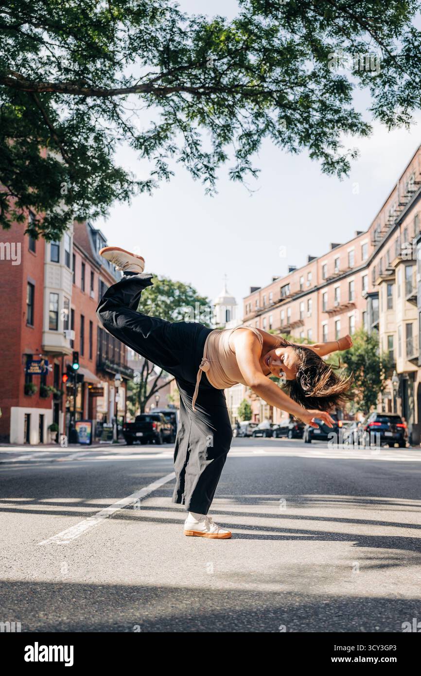 Eine Frau spielt eine dynamische Tanzposition auf einer sonnigen Stadtstraße Stockfoto