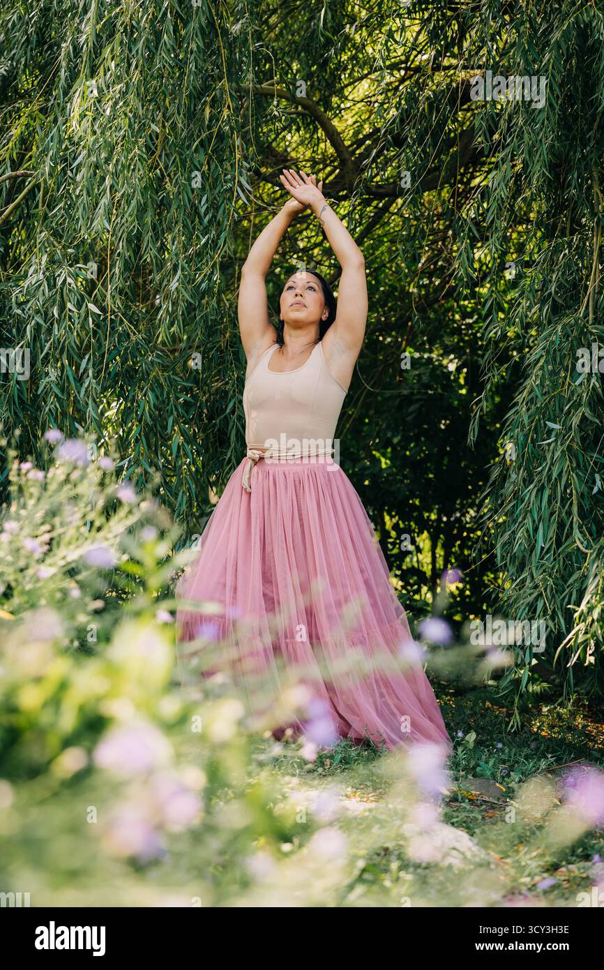 Frau, die mit erhobenen Armen unter Weiden im Garten steht Stockfoto