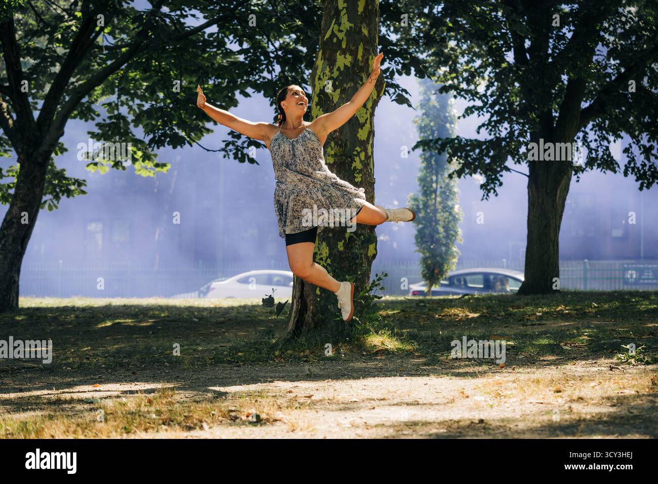 Fröhliche Frau springt im Sonnenlicht unter Bäumen in einem nebeligen Park Stockfoto