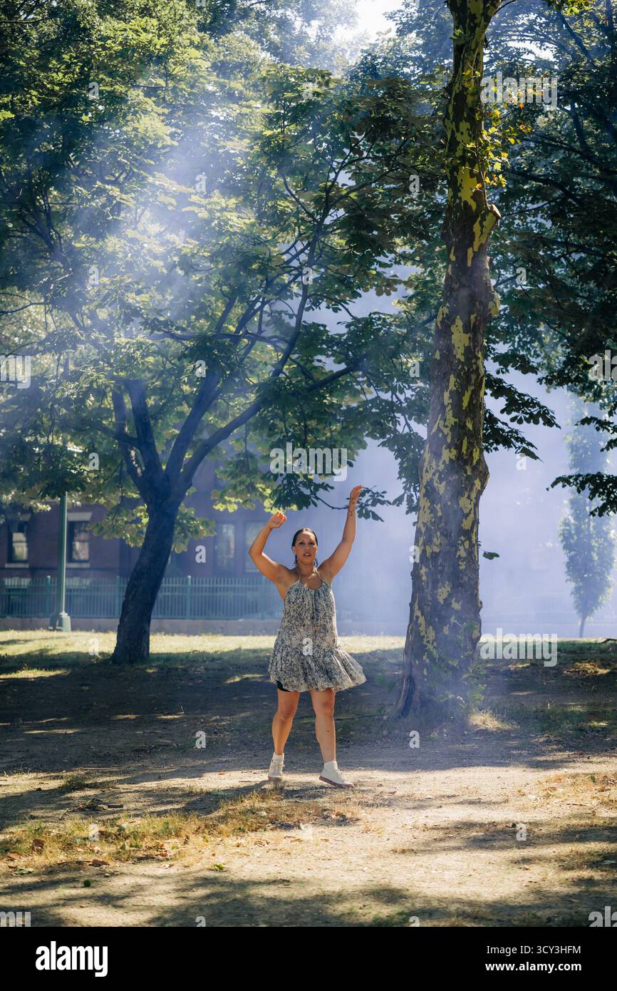 Frau tanzt spontan im sonnendurchfluteten Park mit Rauch Stockfoto