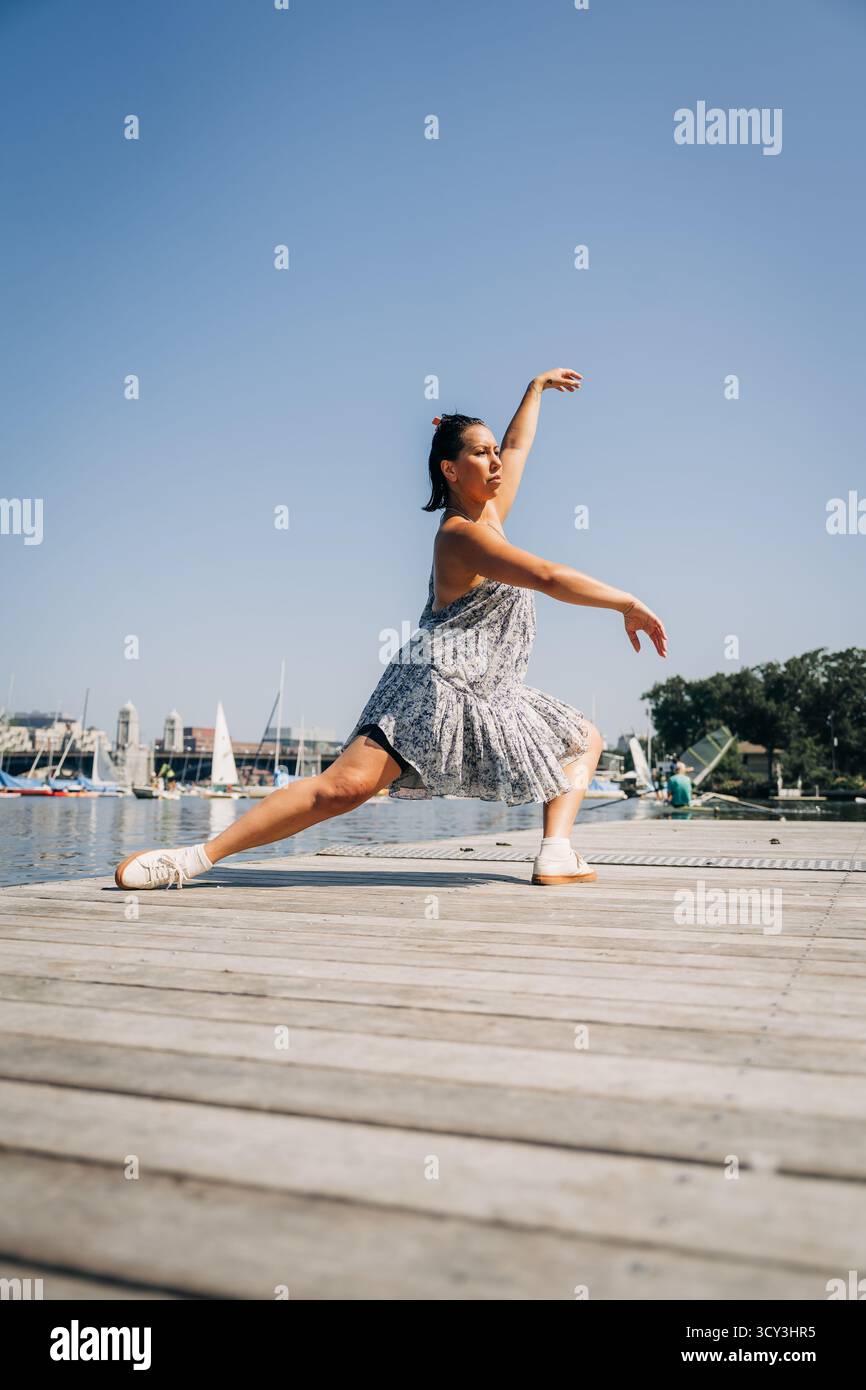 Eine Frau spielt eine tiefe Longe-Tanz-Pose auf dem Dock am Wasser Stockfoto