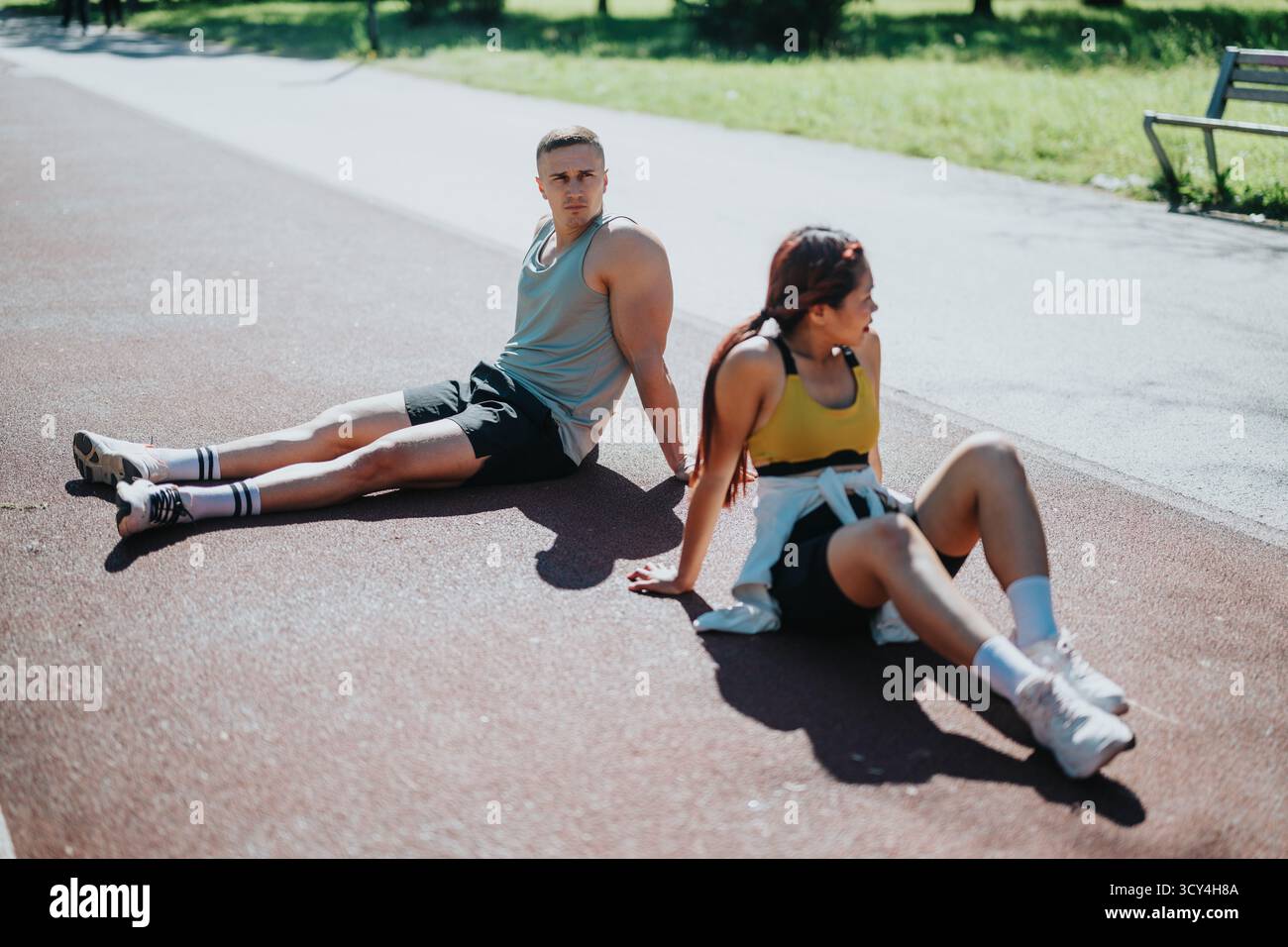 Fittes Paar, das sich nach dem Joggen an einem sonnigen Tag im Park im Freien ausruhen lässt Stockfoto
