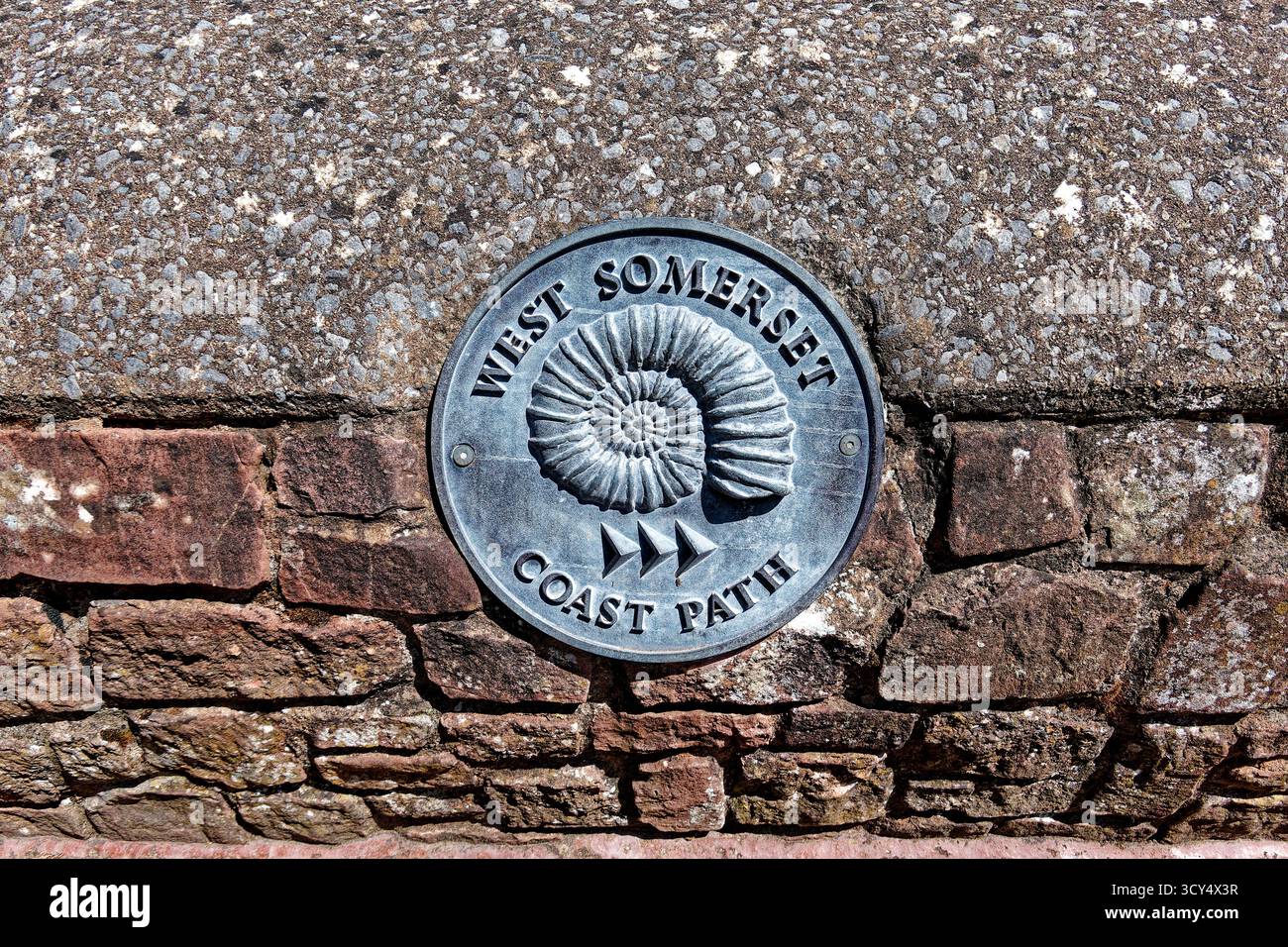 Minehead, Somerset, England, Vereinigtes Königreich - 28. Mai 2025: Ein Schild am West Somerset Coast Path, das in einer Mauer angebracht ist, die einen Ammoniit darstellt, und sich in der Nähe des Hafens von Minehead befindet Stockfoto