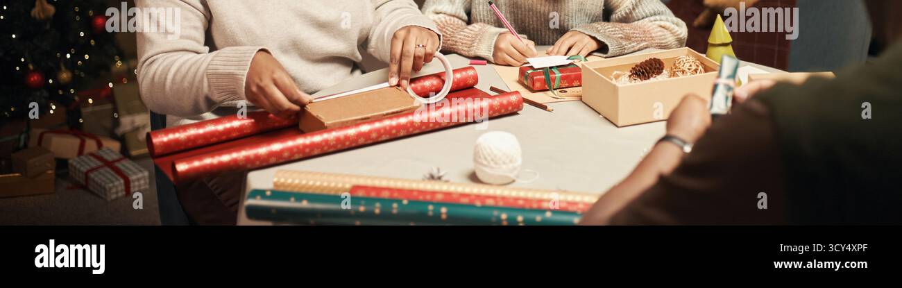 Kaukasierin mittleren Alters und junge Erwachsene Kaukasierin, die Weihnachtsgeschenke und Schreibkarten am Tisch mit Papierrollen und Weihnachtsdekorationen in festlicher Atmosphäre einhüllt Stockfoto