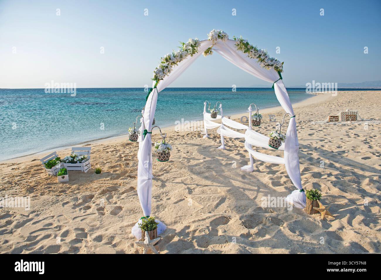 Einrichtung des Hochzeitsgangs am Hochzeitstag mit weißen Vorhängen und Bogen auf einem sandigen tropischen Strandparadies zum offenen Ozean Hintergrund Stockfoto