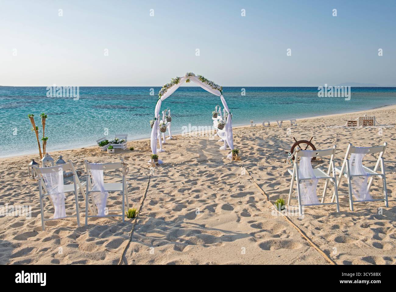 Einrichtung des Hochzeitsgangs am Hochzeitstag mit weißen Vorhängen und Bogen auf einem sandigen tropischen Strandparadies zum offenen Ozean Hintergrund Stockfoto