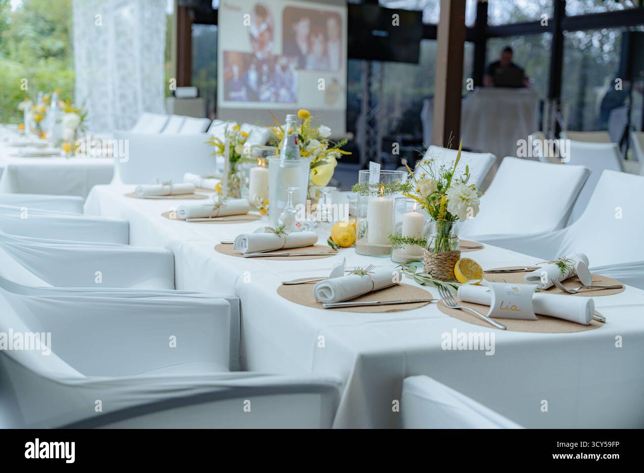 Der Tisch für den Hochzeitsempfang ist elegant mit Blumenarrangements und Kerzen eingerichtet und schafft eine elegante Atmosphäre. Teller und Besteck ordentlich angeordnet Stockfoto