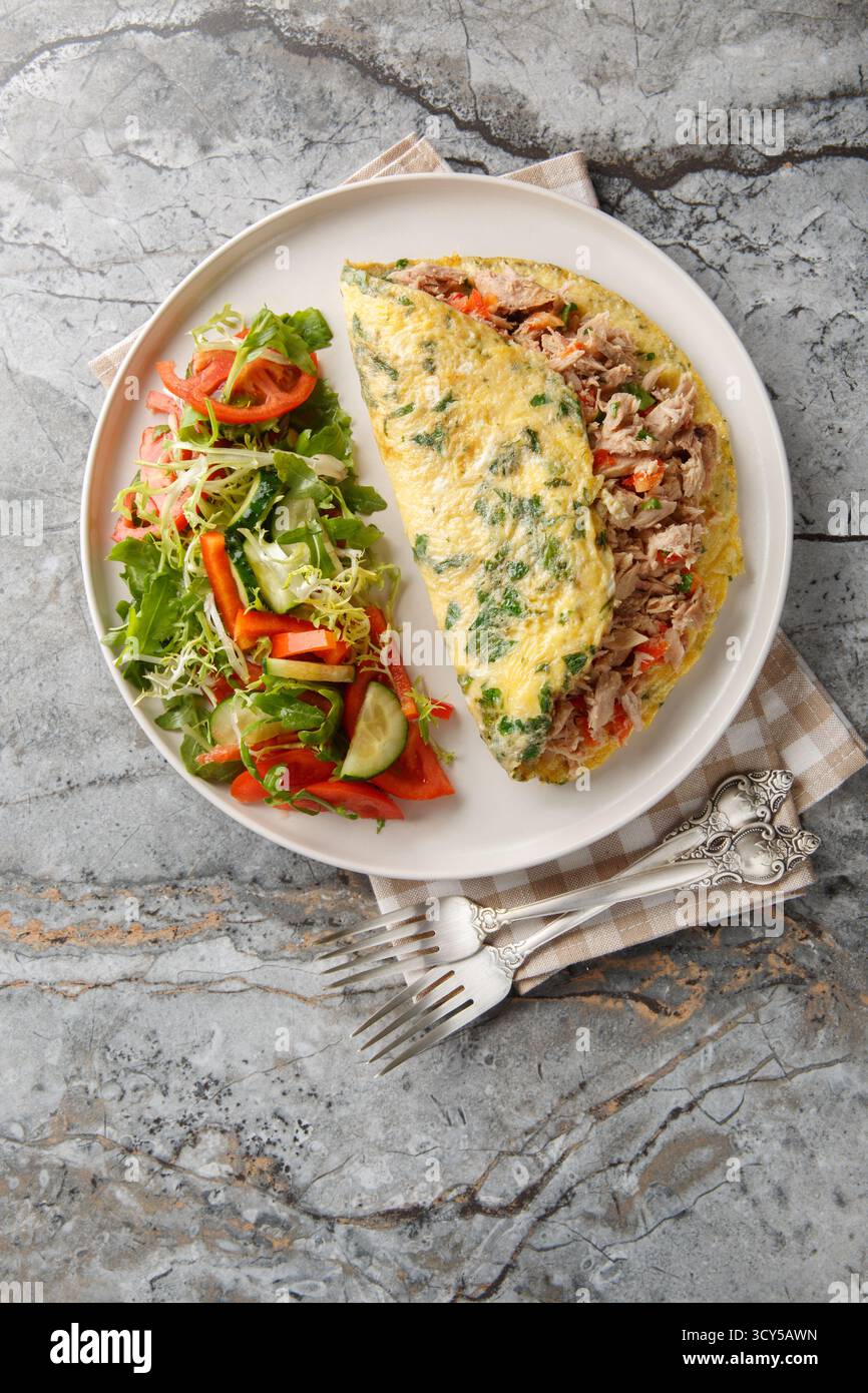 Frühstücksomelette mit Dosenthunfisch und frischem Gemüsesalat in der Nähe auf dem Teller auf dem Tisch. Vertikale Draufsicht von oben Stockfoto