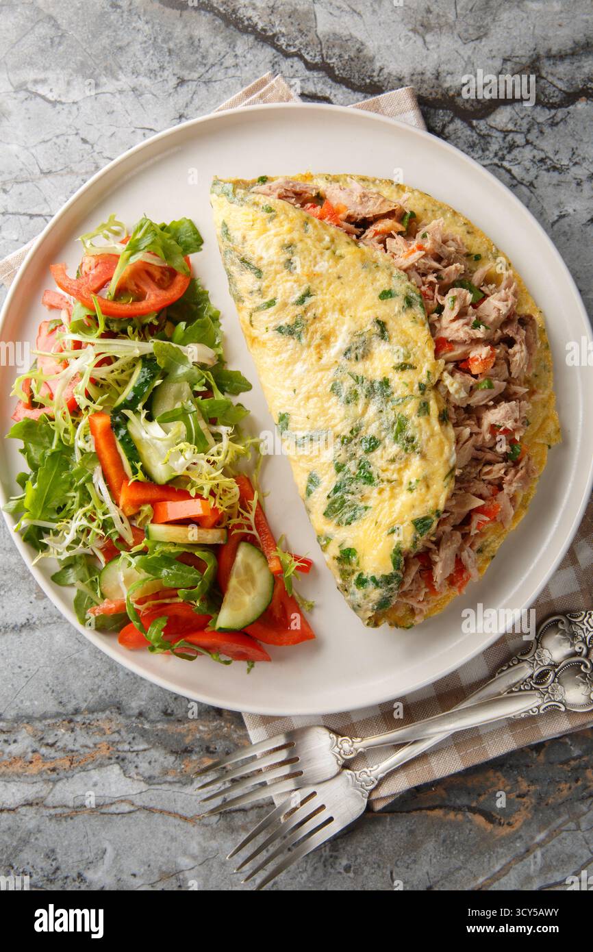 Spanisches Thunfischomelette mit Gemüsesalat in Nahaufnahme auf einem Teller auf dem Tisch. Vertikale Draufsicht von oben Stockfoto
