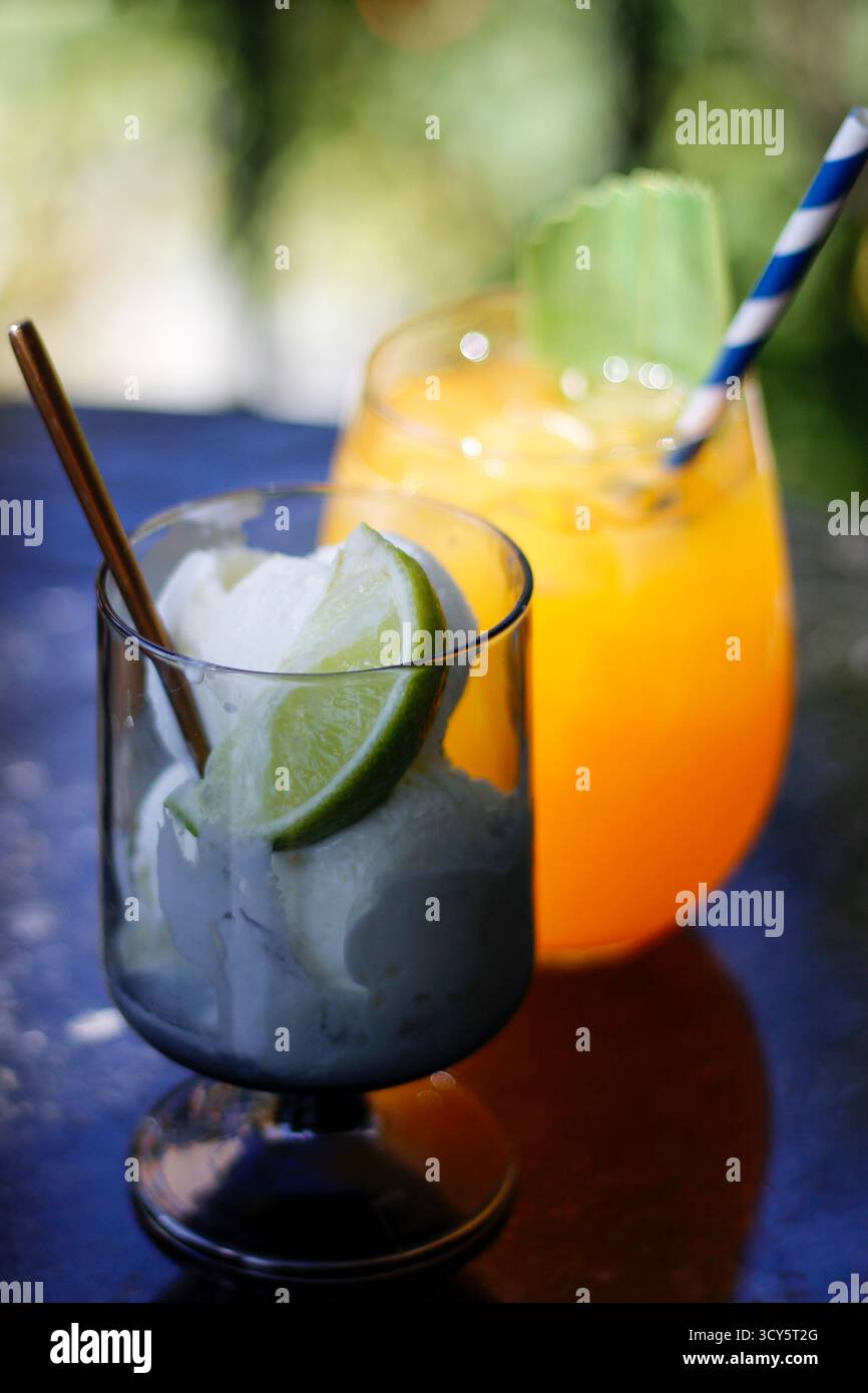 Zwei erfrischende Sommergetränke auf einem Tisch, einer mit Orangensaft und der andere mit Limette und Schlagsahne. Hochwertige Fotos Stockfoto