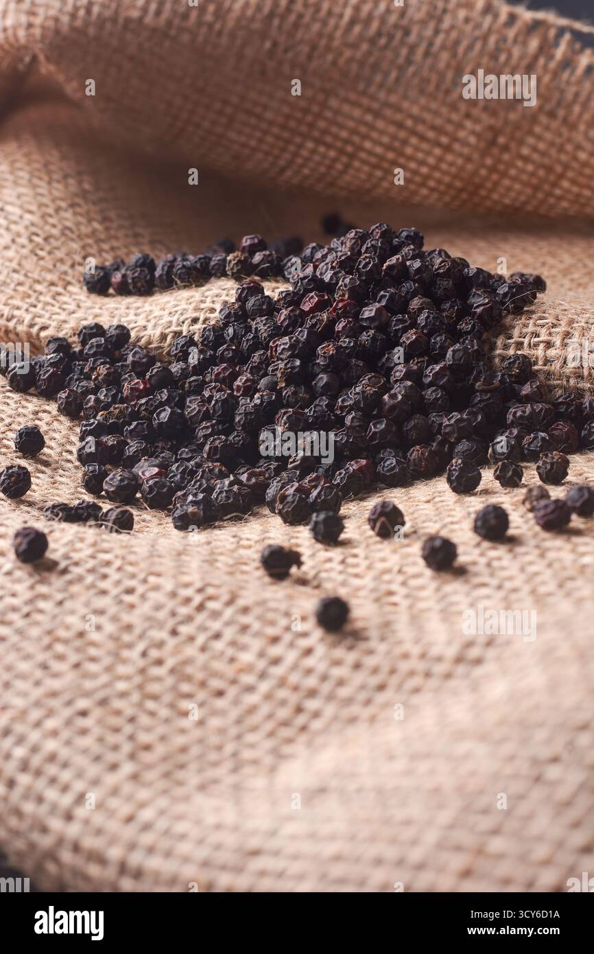 Nahaufnahme von schwarzen Pfefferkörnern auf Sackleinen, dunklen Gewürzen auf einem rustikalen gewebten Sack mit warmer Beleuchtung, natürlichen Zutaten und kulinarischem Gewürzkonzept Stockfoto