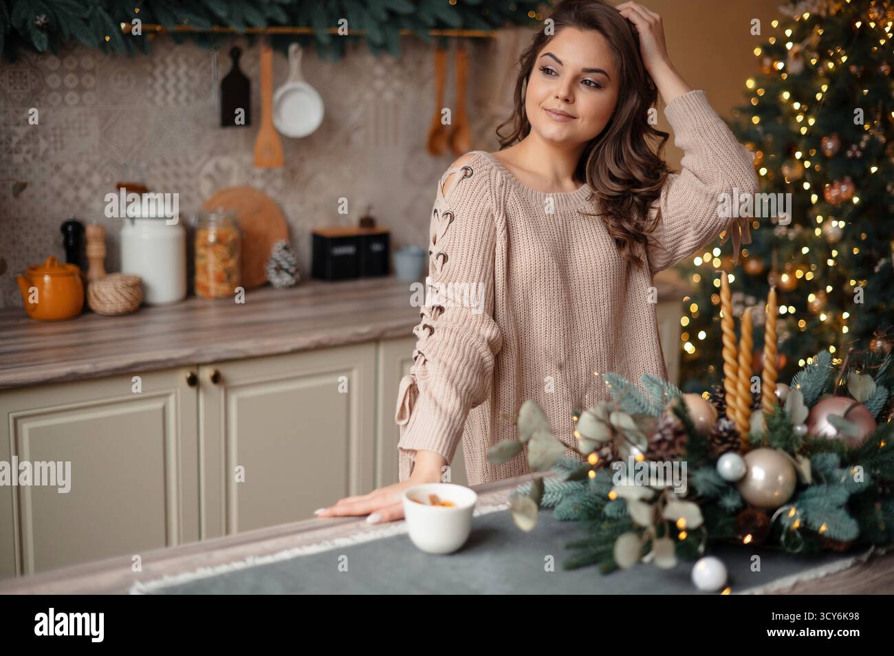 Frau in gemütlicher Küche mit Weihnachtsdekor, mit Strickpullover. Stockfoto
