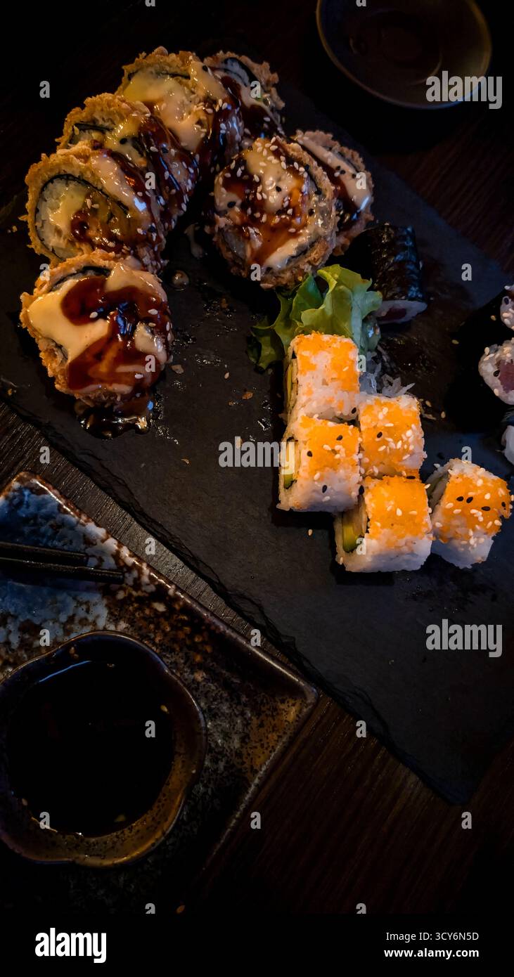 Verschiedene japanische Sushi-Brötchen mit Soße auf schwarzem Schieferteller im Restaurant. Stockfoto