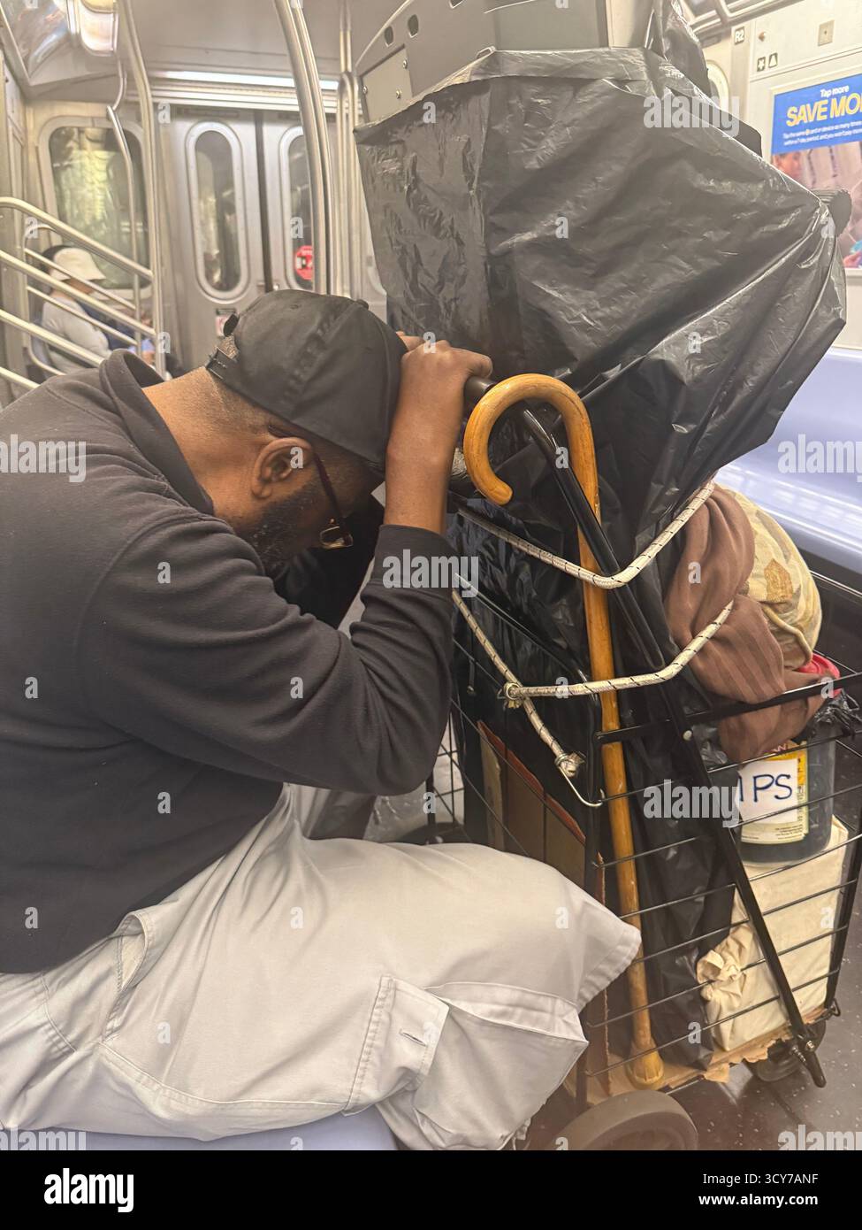 Ein müder Mann fährt in New York City mit einem Wagen voller Sachen und einem Stock in der U-Bahn. Stockfoto