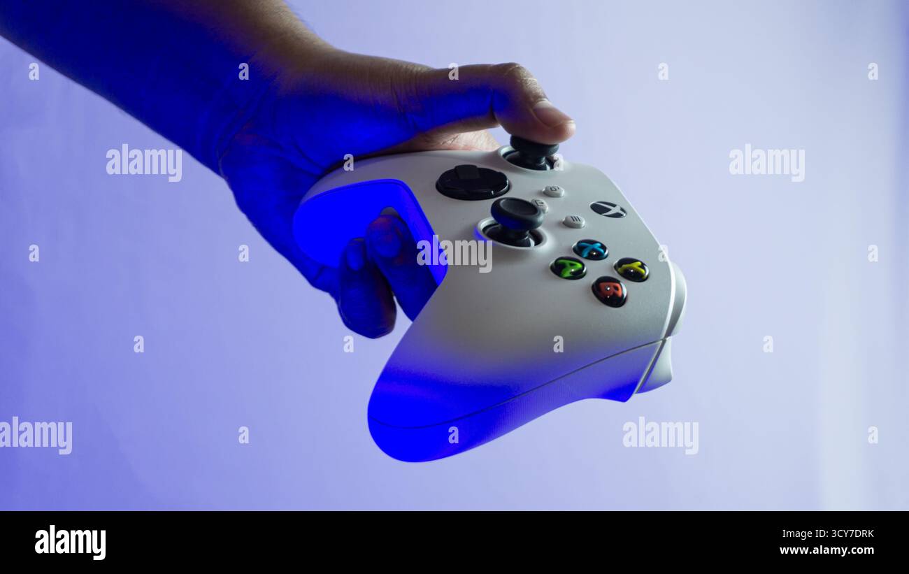 South Kalimantan, Indonesien - 07 14 2025 : weißer S|X-Controller der Xbox-Serie in einer Hand gehalten auf weißem Hintergrund unter blauem Umgebungslicht, zeigt min Stockfoto