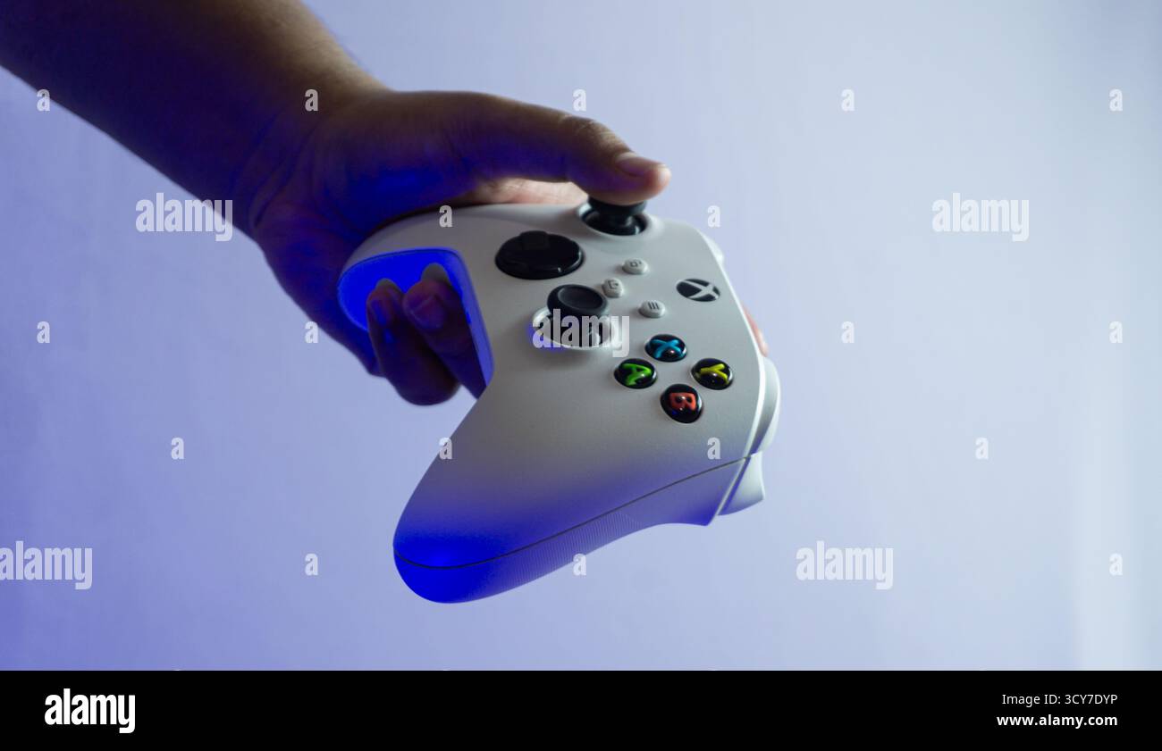 South Kalimantan, Indonesien - 07 14 2025 : weißer S|X-Controller der Xbox-Serie in einer Hand gehalten auf weißem Hintergrund unter blauem Umgebungslicht, zeigt min Stockfoto