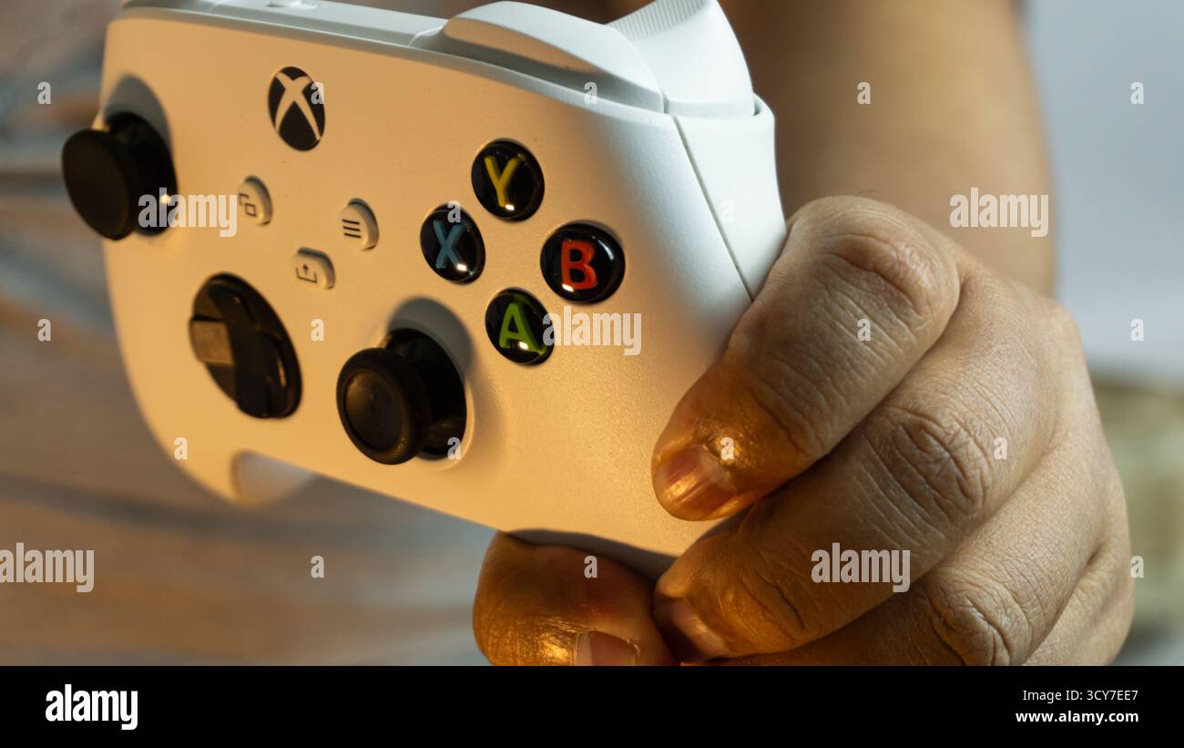 Süd-Kalimantan, Indonesien - 07 14 2025 : eine Hand hält den weißen Controller der Xbox Serie S|X auf sauberem Hintergrund unter weichem, warmem Licht, wodurch es gemütlich wird Stockfoto