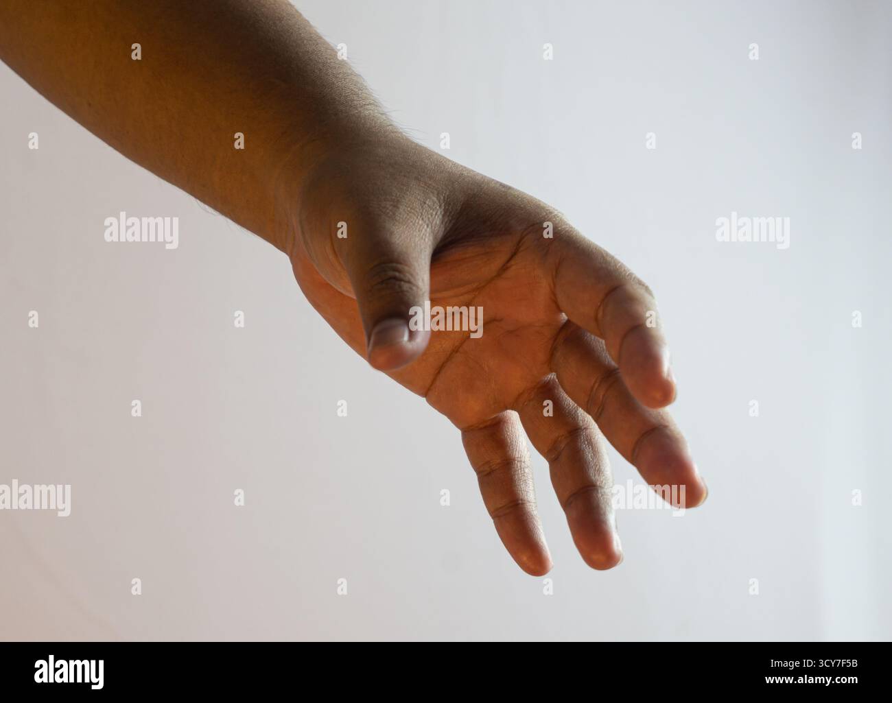 Männliche Hand mit weit geöffneten Fingern auf weißem Hintergrund mit warmer Umgebungsbeleuchtung, einladender und ausdrucksstarker Geste in einfacher, neutraler Studioeinrichtung Stockfoto
