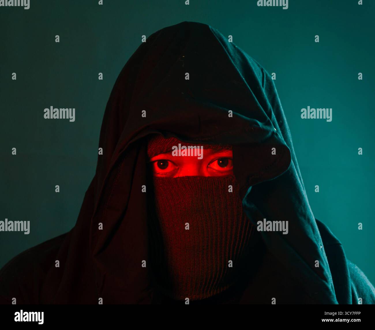 Männliche Figur komplett mit roter und grüner Beleuchtung auf schwarzem Hintergrund bedeckt, geheimnisvolle Ninja-ähnliche Präsenz mit versteckter Identität und Spannung Stockfoto