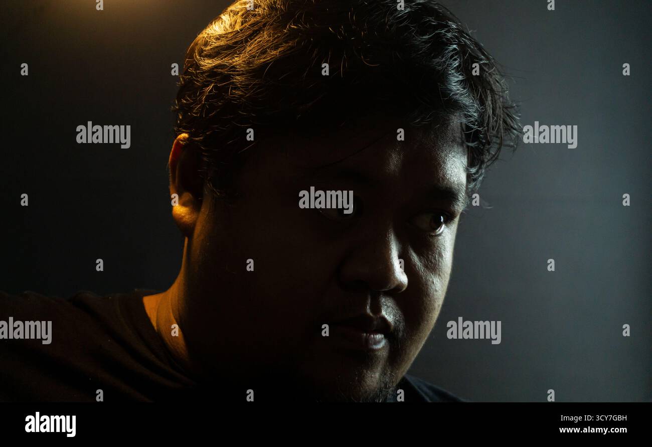 Nahaufnahme des männlichen Gesichtes mit warmem Umgebungslicht, das die Hautstruktur vor dunklem Hintergrund unterstreicht, dramatisches, geheimnisvolles Porträt mit leiser Spannung und Geheimhaltung Stockfoto