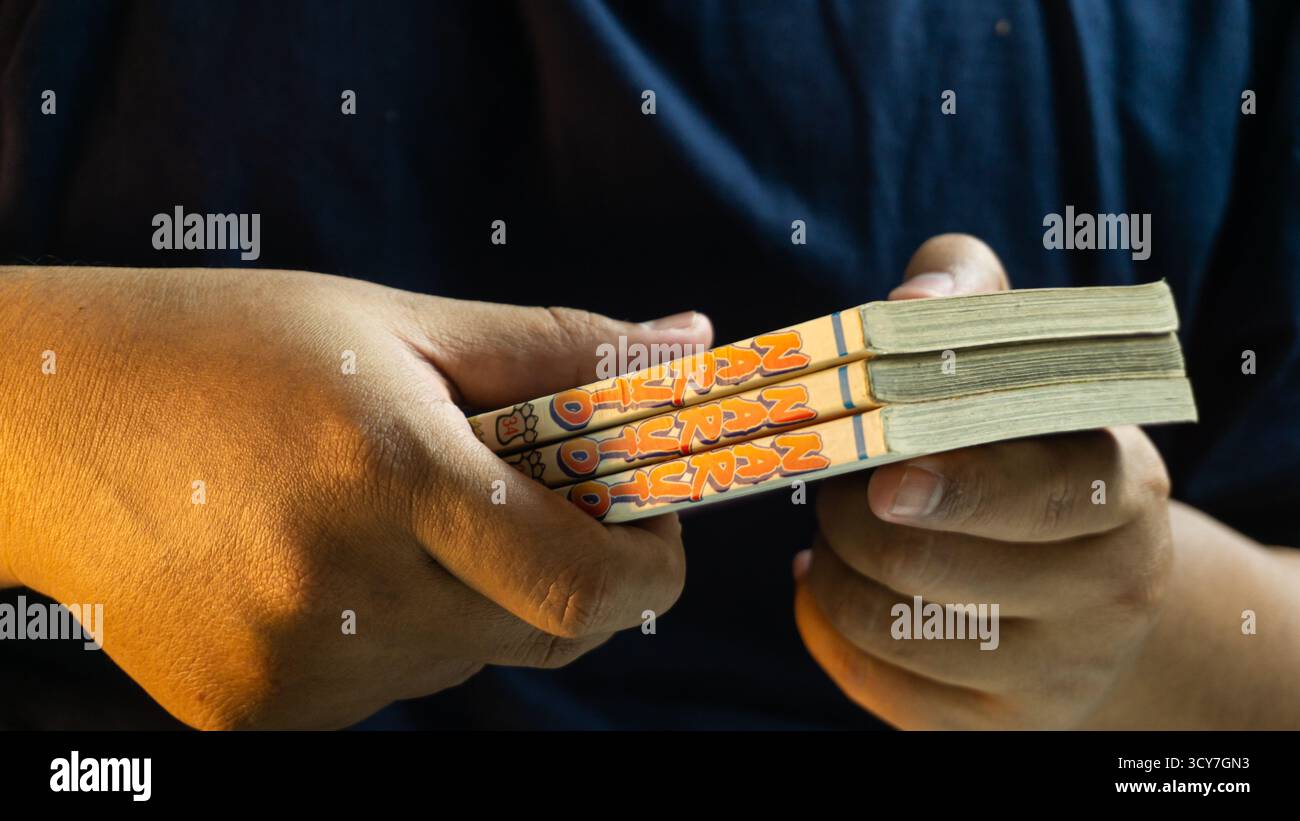 South Kalimantan, Indonesien - 07 21 2025 : geschlossenes Naruto-Manga-Buch, gehalten von männlicher Hand unter warmem Umgebungslicht, mit Cover-Artwork und persönlichem Inhalt Stockfoto