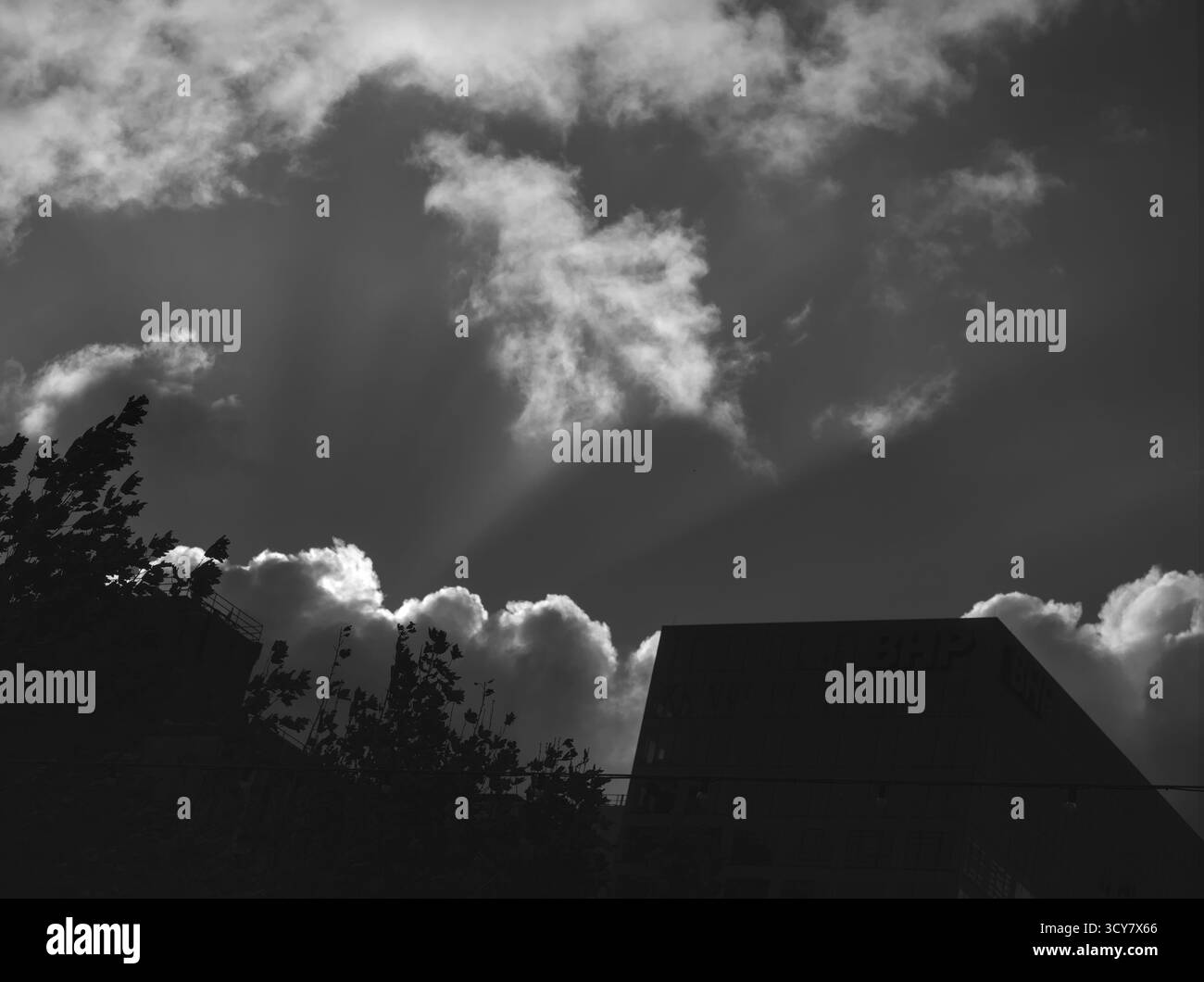 Dramatische schwarz-weiße Silhouette der Stadt mit hellen Sonnenstrahlen, die dunkle Wolken durchdringen; kraftvolle, geheimnisvolle Stimmung. Stockfoto