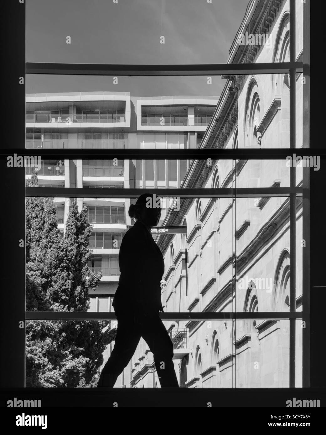 Ein Geschäftsmann mit Silhouette geht an historischen und modernen Gebäuden vorbei; kontrastreiches Schwarz-weiß, dynamisch, entschlossen. Stockfoto