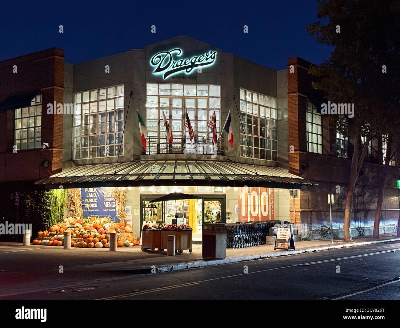 Blick von außen auf das Dräger's Market Supermarkt mit saisonaler Kürbisausstellung, leuchtendem Schild und geparkten Einkaufswagen - Menlo Park Stockfoto