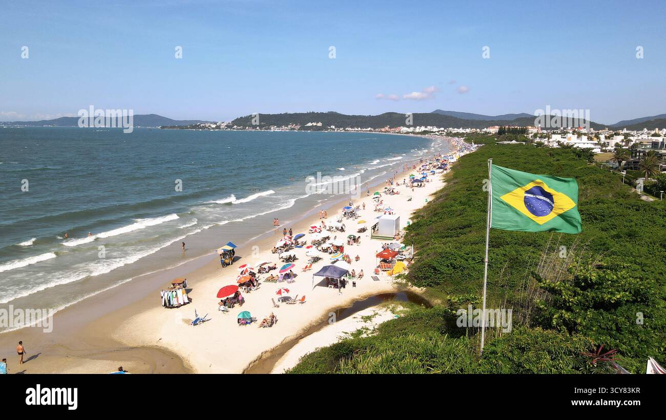 Luftbild der brasilianischen Flagge, die im Wind flattert, am Strand Jurere Internacional in Florianópolis, Santa Catarina, mit dem Strand voller p Stockfoto