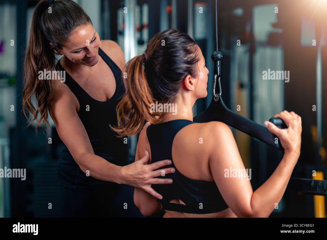 Fitnesstrainer, der eine Frau mit einem Lat-Pulldown-Gerät im Fitnessstudio trainiert. Stockfoto