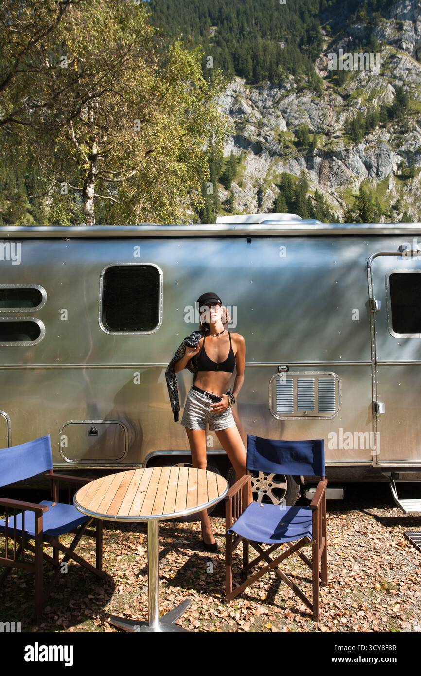 Schöne schlanke Frau mit cooler Attitüde, die vor silbernem Stoßfänger steht. Modische Frau vor einer Reise im Vintage- oder modernen Retro-Stil Stockfoto Schöne schlanke Frau mit cooler Attitüde, die vor silbernem Stoßfänger steht. Modische Frau vor einer Reise im Vintage- oder modernen Retro-Stil Stockfoto