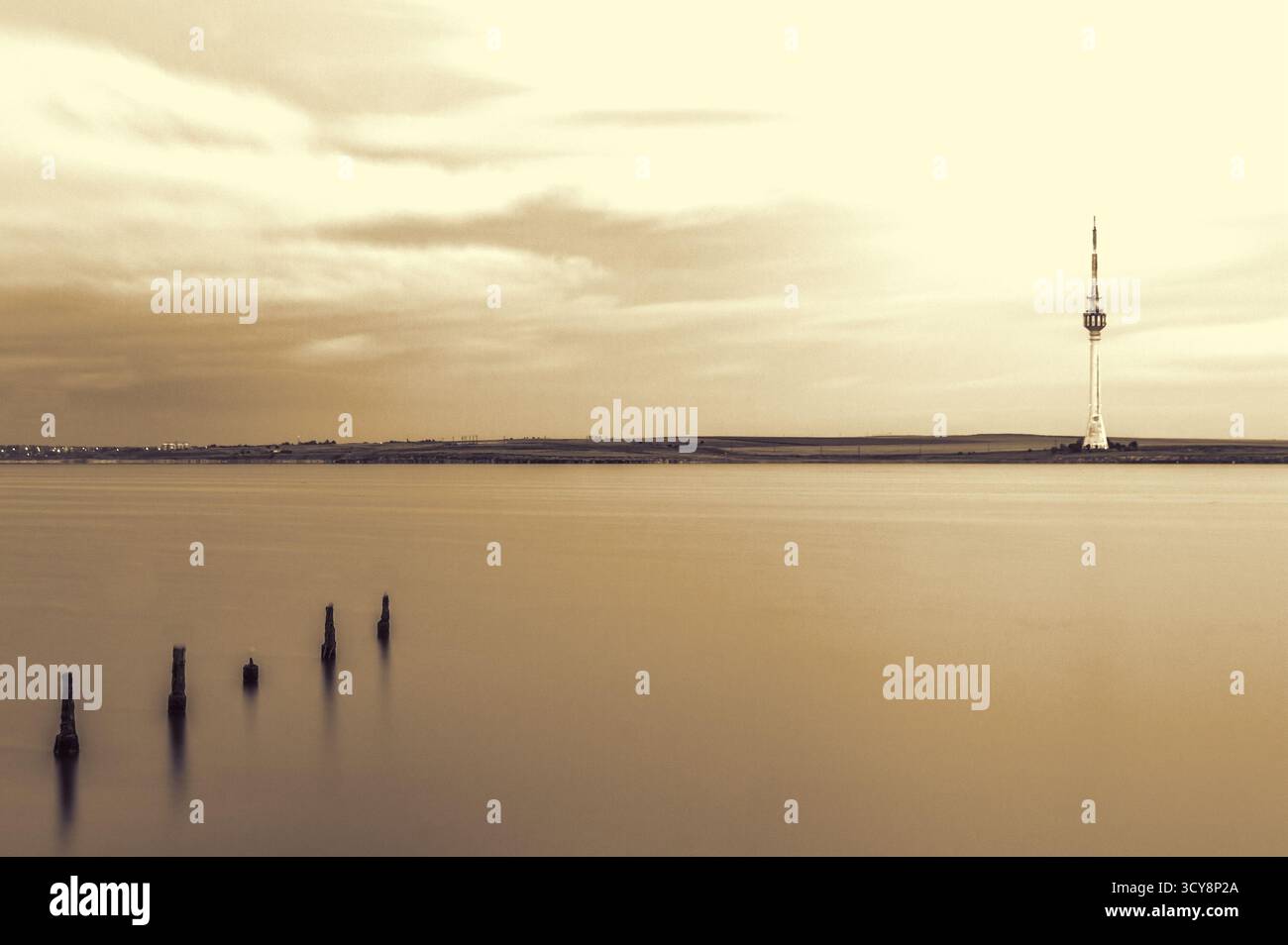 Langzeitbelichtung des ruhigen Sees in Rumänien. Sepia-Töne und verwitterte Holzpfosten erinnern an Ruhe und Zeitlosigkeit. Stockfoto