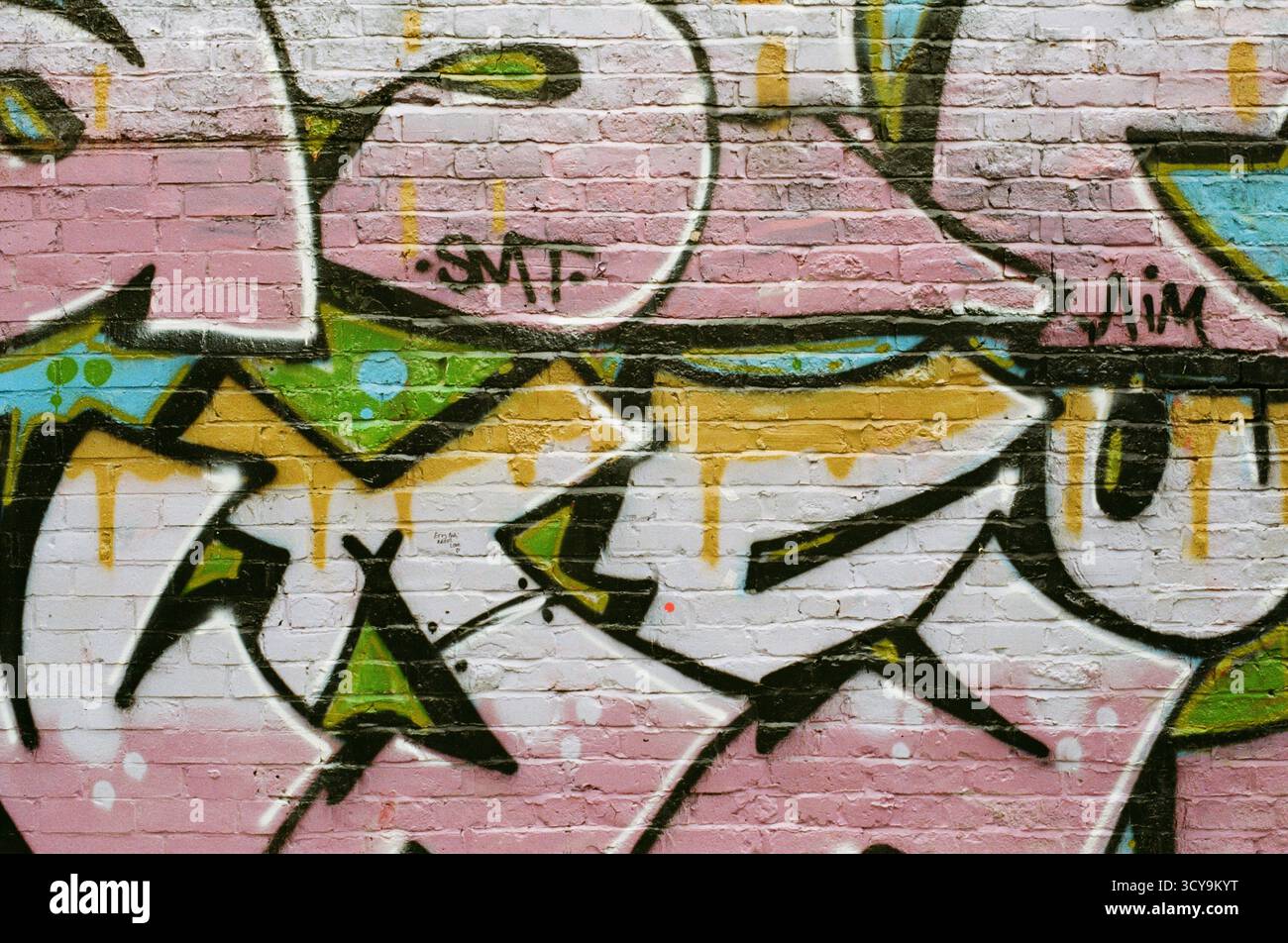 Pinkfarbene Graffiti-Kunstwerke an einer Ziegelwand in Manchester, England, fotografiert auf dem Fujifilm 200 Farbfilm, mit auffälligen Street-Art-Details und Texturen Stockfoto