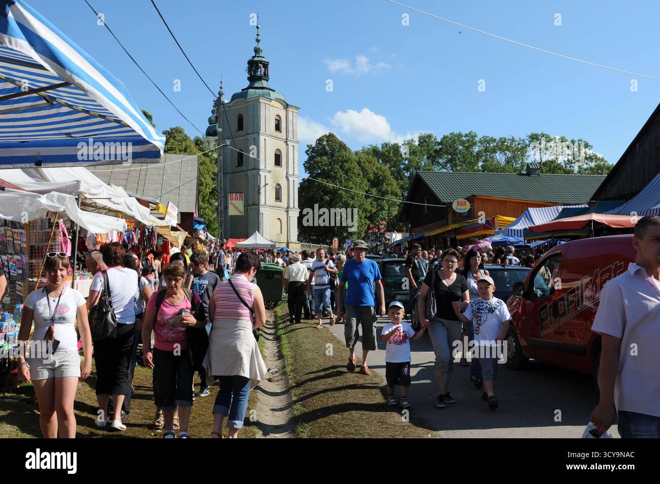Familien und Pilger, die an Ständen in der Nähe des Kirchturms während der Himmelfahrt in Kalwaria Pacławska im Südosten Polens spazieren, Stockfoto