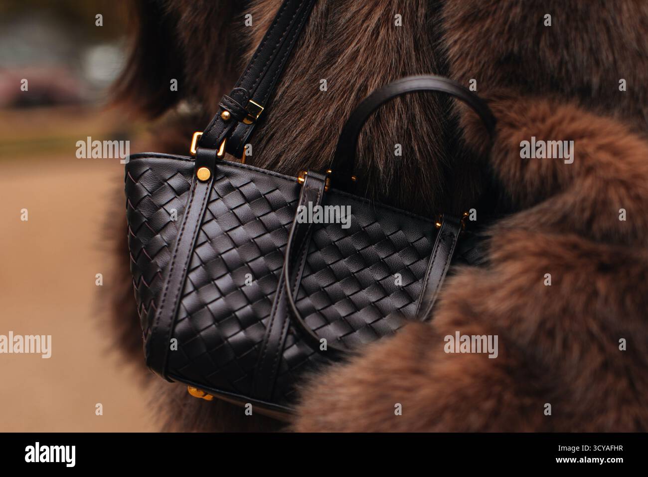 Brauner Pelzmantel und trendige Handtasche aus gewebtem Leder, modische Details des lässigen Outfits für Damen im Herbst Stockfoto