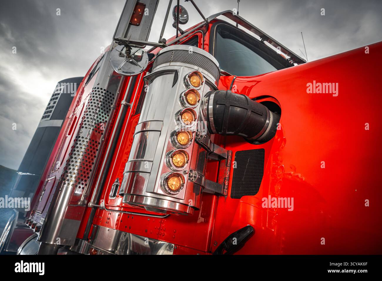 Ein leuchtend roter Lkw zeigt seine polierten Chromakzente am Nachmittag unter einem dramatischen Himmel. Stockfoto