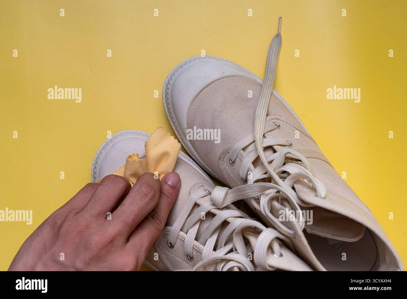 Beigefarbener Canvas-Stiefel, der im Studio mit den Händen vor hellgelbem Hintergrund gereinigt wird Stockfoto