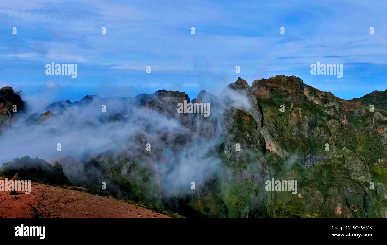 Neblige Berglandschaft mit dramatischen Klippen, Morgenlicht und rötlichen Felsen. Ätherische Wolken treiben durch grüne Täler. Perfekt für die Natur, Trav Stockfoto