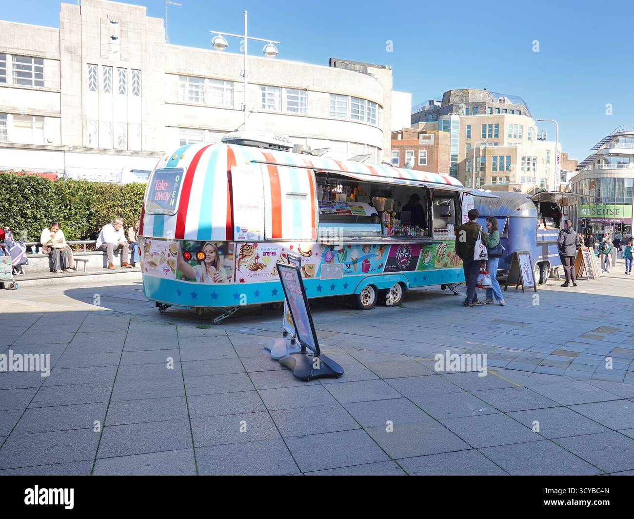 Street Food-Anbieter arbeiten mit umgebauten Airstream Caravans im Stadtzentrum von Brighton, England. Silberne Anhänger im Retro-Stil, in denen Speisen serviert werden Stockfoto