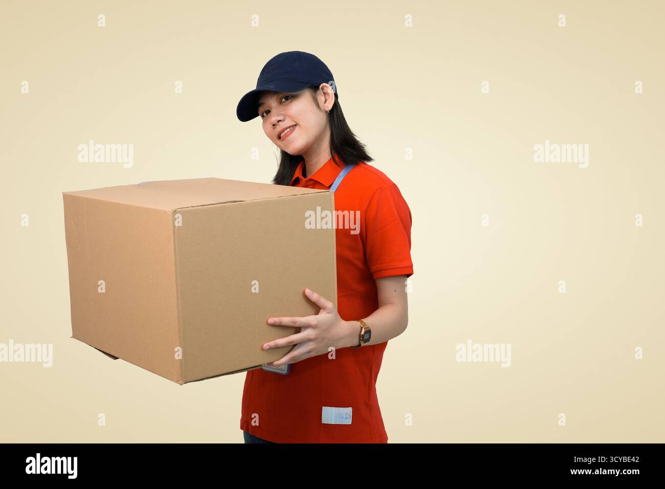 Glückliche Lieferfrau in roter Uniform, die einen großen Karton für den Versand hält Stockfoto