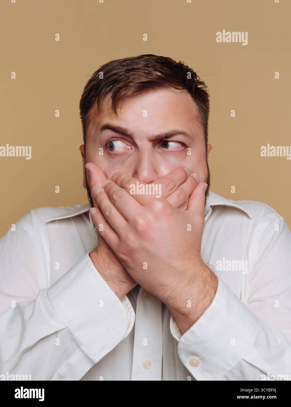 Ein Mann bringt Überraschung und Besorgnis zum Ausdruck, indem er seinen Mund mit den Händen bedeckt. Er schaut seitlich mit breiten Augen vor einem schlichten Hintergrund und schafft eine zehn Stockfoto