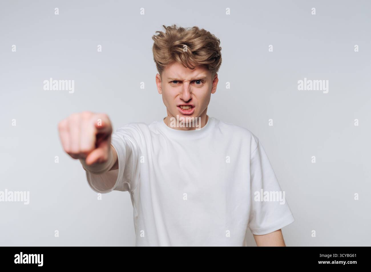 Ein junger Mann mit zerzausten blonden Haaren zeigt sichtbare Wut und Frustration. Er weist darauf hin, als ob er eine starke Aussage oder ein starkes Argument abgibt Stockfoto Ein junger Mann mit zerzausten blonden Haaren zeigt sichtbare Wut und Frustration. Er weist darauf hin, als ob er eine starke Aussage oder ein starkes Argument abgibt Stockfoto