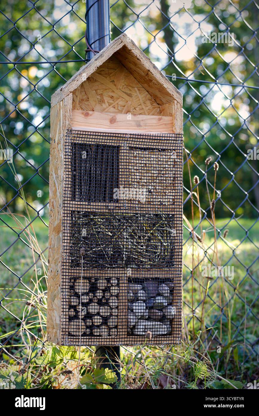Handgefertigtes Insektenhotel mit Vogelfutter auf Gartenzaun, gefüllt mit Pappe, Steinen, Heu, Holz und Sägemehl, Bereitstellung von Unterkünften für Bestäuber Stockfoto