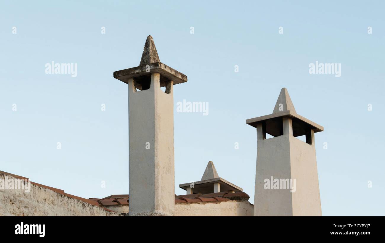 Schornsteine und Lüftungsschlitze auf dem Dach unter dem klaren Himmel auf dem rustikalen Hausdach mit verwittertem Mauerwerk Stockfoto