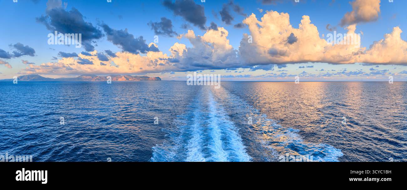 Ein Blick auf die sizilianische Küste in der Nähe von Palermo bei Sonnenaufgang, mit orangefarbenen Wolken, die sich im Meer spiegeln und von einer Schiffswache durchzogen werden, Italien. Stockfoto