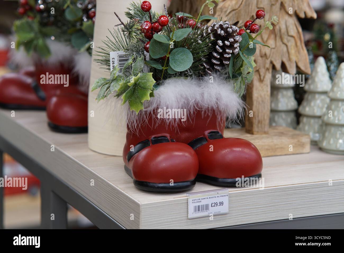 Rote Weihnachtsmannstiefeldekoration gefüllt mit Tannenzapfen, Beeren und Grün auf festlichen Ausstellungen im Haskins Garden Centre. Haskins Garden Centre, Snowhill Stockfoto